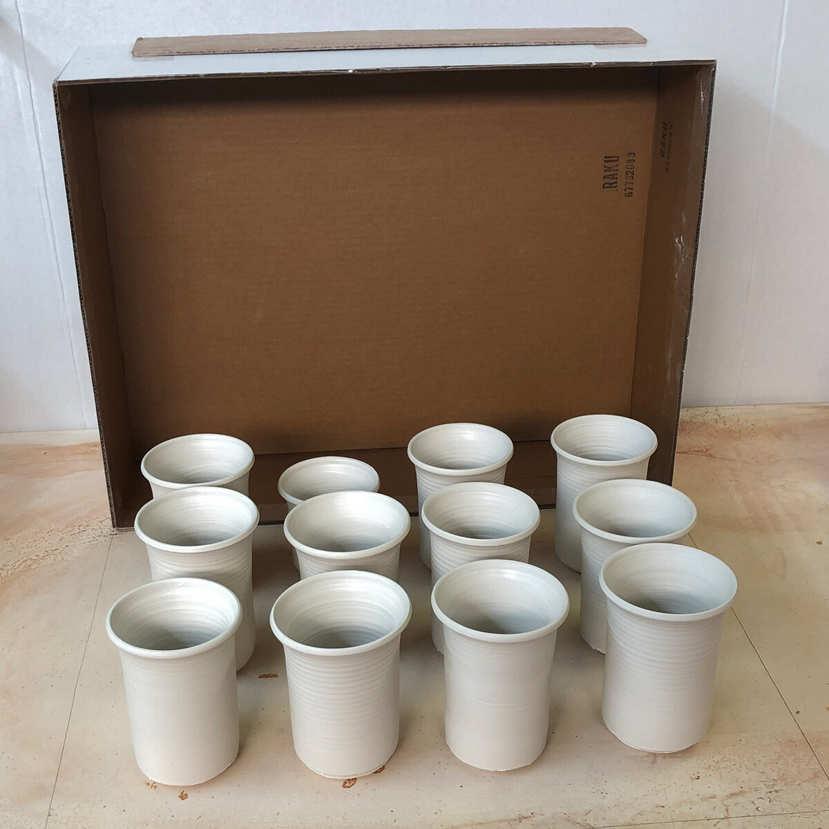 Freshly thrown porcelain mugs placed on a plaster table and being covered by a wax-lined box Freshly thrown porcelain mugs placed on a plaster table and being covered by a wax-lined box