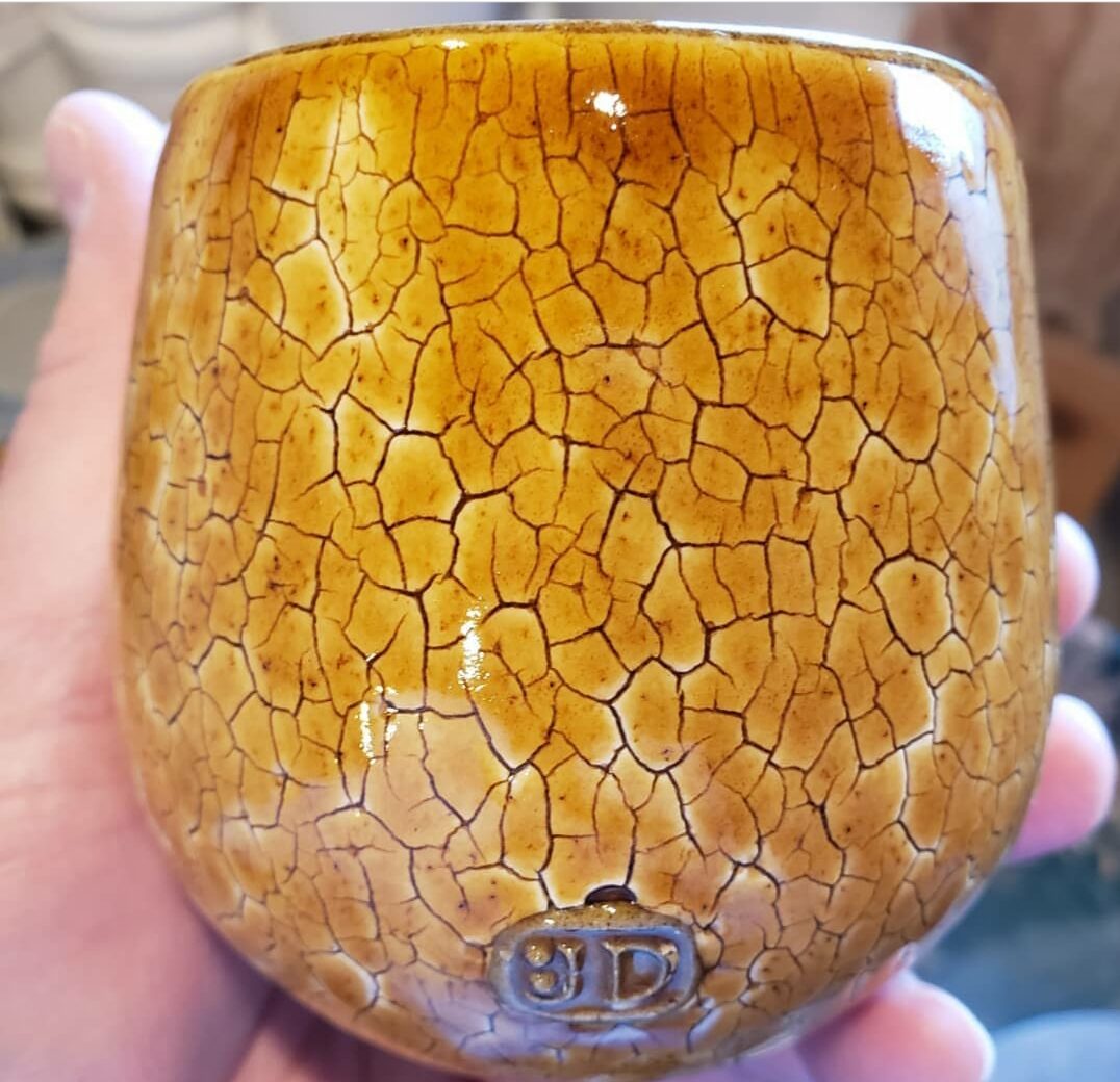 A pottery mug with a honey over-glaze that highlights an engobe having a decorative crack pattern A pottery mug with a honey over-glaze that highlights an engobe having a decorative crack pattern